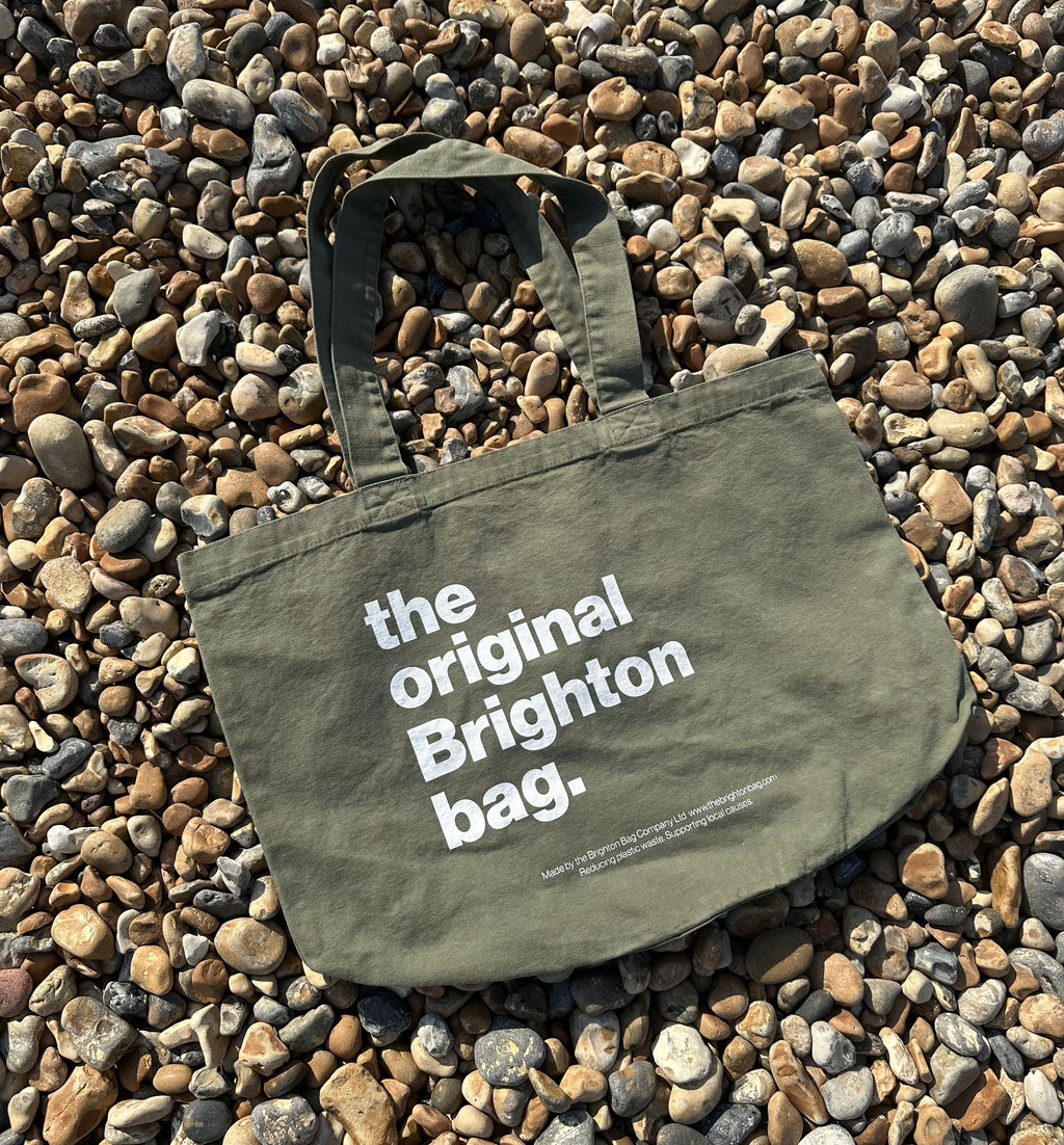 Green tote bag with 'the original Brighton bag' text on pebbles