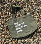 Green tote bag with 'the original Brighton bag' text on pebbles