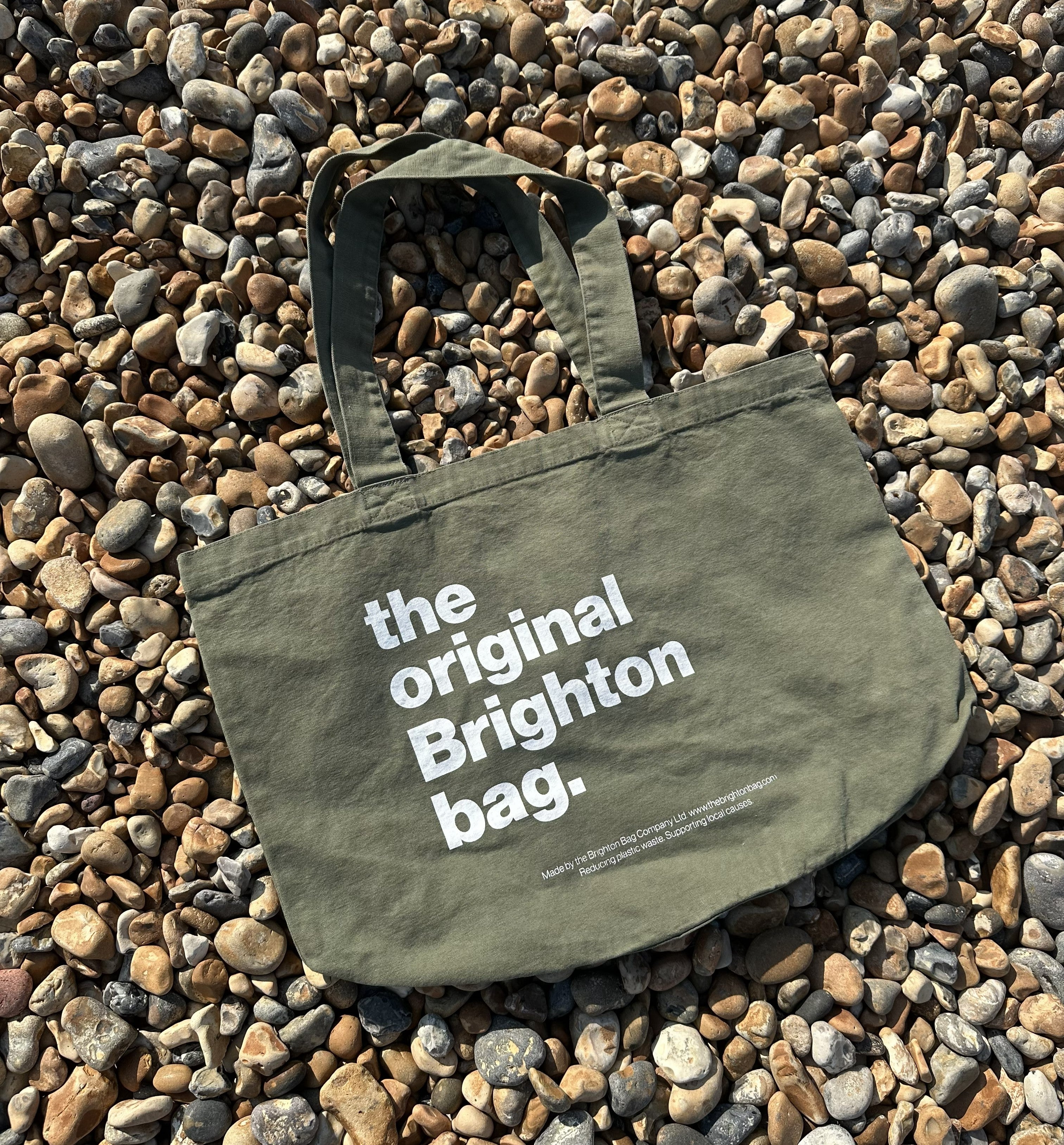 Green tote bag with 'the original Brighton bag' text on pebbles