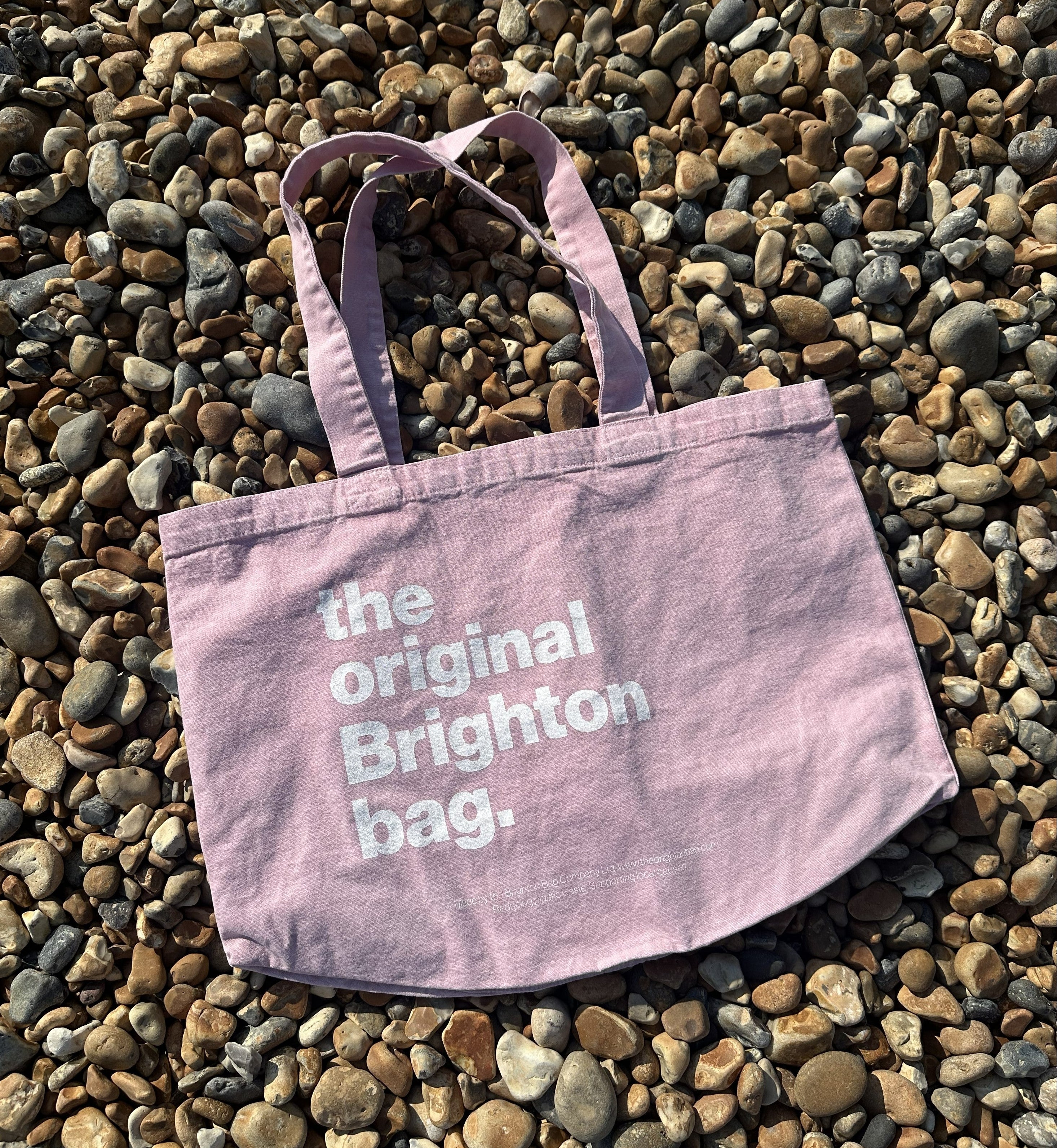 Pink tote bag with 'the original Brighton bag' text on pebbles