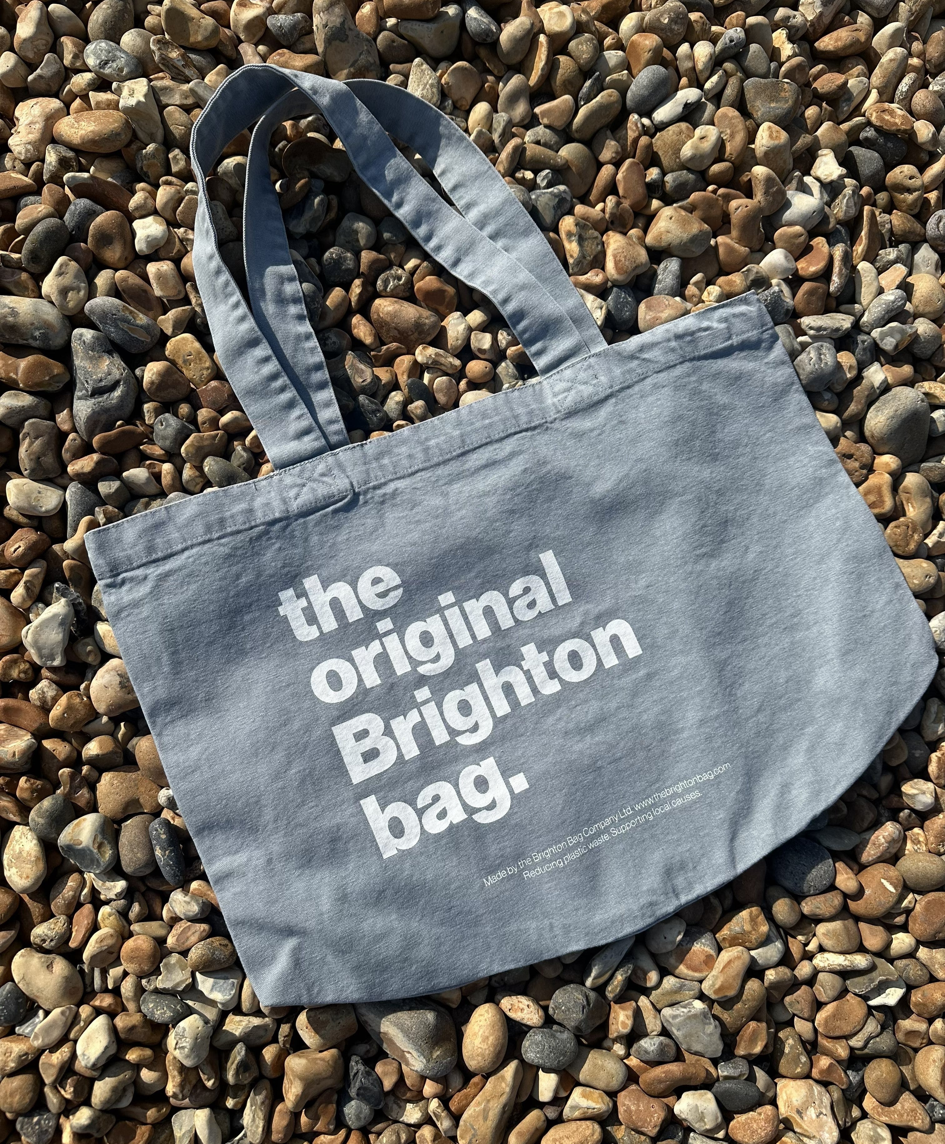 Blue tote bag with 'the original Brighton bag' text on pebbles